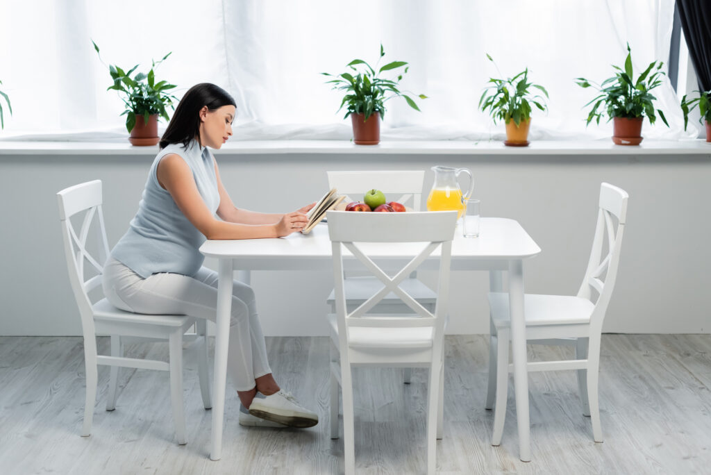 woman at white table relaxing for health with green plants and white table