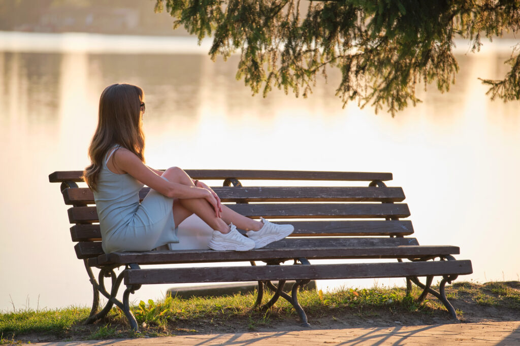 The Surprising Truth: Physical Pain Disrupts Presence & Clarity woman sitting on a lake-side bench during a warm summer evening beautifully captures a mood of solitude, reflection, and calm presence
