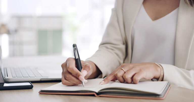 woman in beige business jacket writing in open journal with black quality pen